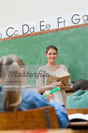 Smiling teacher holding book next to board