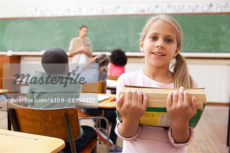 Schoolgirl holding pile of books in classroom