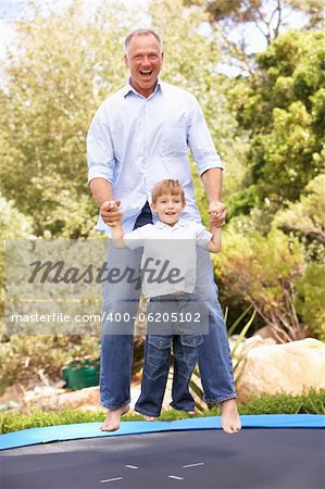 Father And Son Jumping On Trampoline In Garden