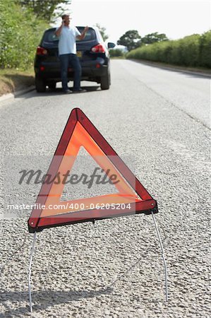 Driver Broken Down On Country Road With Hazard Warning Sign In Foreground