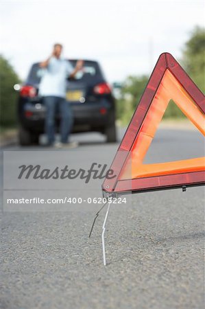 Driver Broken Down On Country Road With Hazard Warning Sign In Foreground