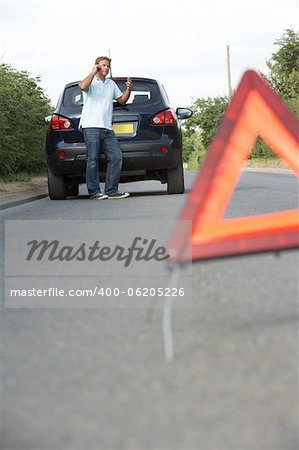 Driver Broken Down On Country Road With Hazard Warning Sign In Foreground