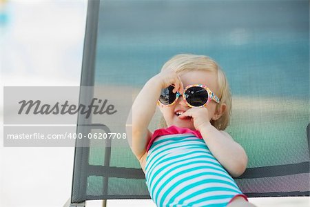 Portrait of baby in swimsuit and sunglasses laying on sunbed