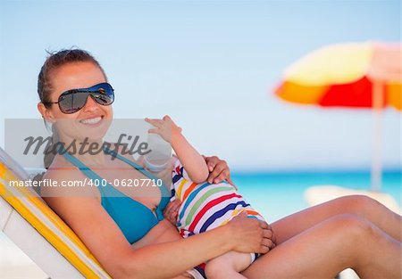 Mother laying on sun bed and holding baby drinking water