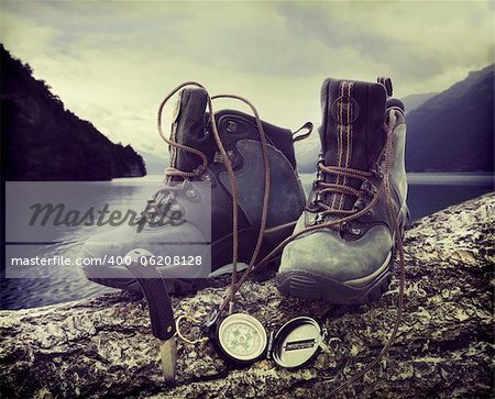 Hiking boots with compass on tree trunk near lake