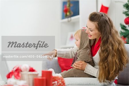 Happy young mother spending Christmas with baby and pointing on laptop