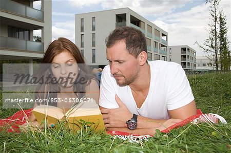 Young couple lying in meadow reading book