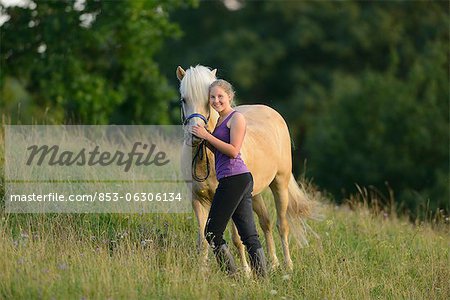 Jeune fille souriante à cheval sur la prairie