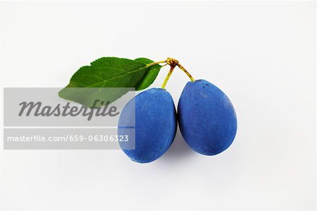 Two damsons on a white surface
