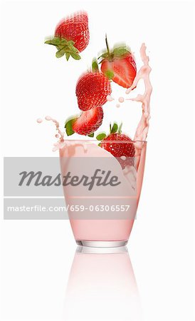 Strawberries falling into a glass of strawberry milk