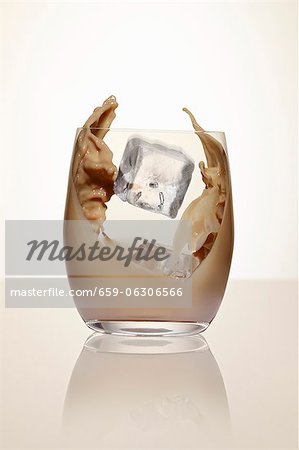 An ice cube falling into a glass of cream liqueur