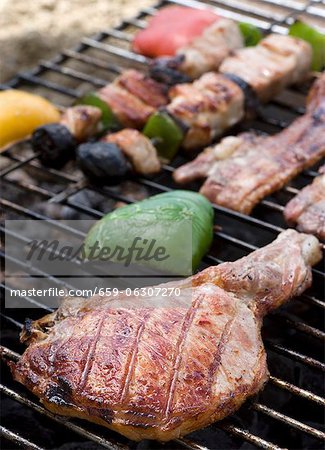 A pork chop, bacon and kebabs on a barbecue