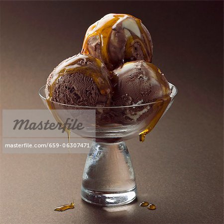Drei Kugeln Schokoladeneis mit Sirup in eine Glasschale Drei Kugeln Schokoladeneis mit Sirup in eine Glasschale