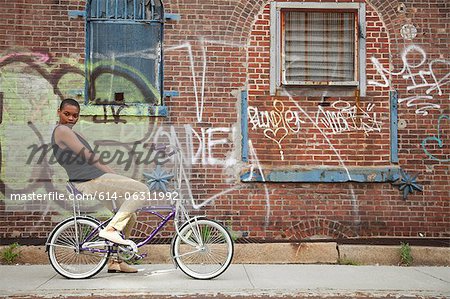 Portrait of a young woman on bicycle by wall covered in graffiti