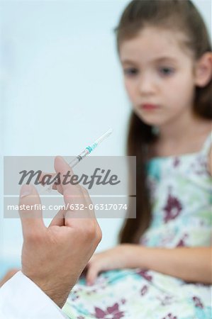 Doctor's hand holding syringe, girl sitting in background