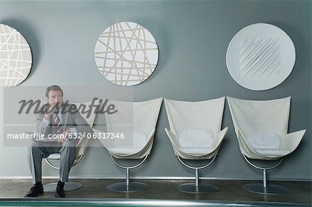 Mature businessman sitting at end of row of chairs in waiting room