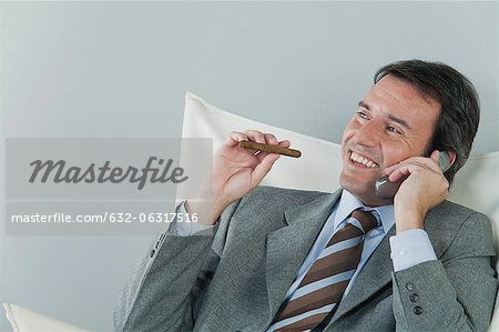 Mature businessman using cell phone and smoking cigar