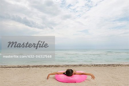 Girl lying on inflatable ring on beach, rear view