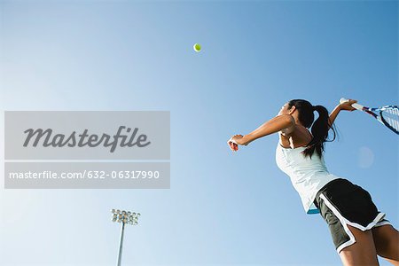 Female tennis player serving ball, low angle view