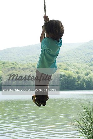 Boy hanging from rope over river, rear view