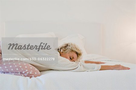 Mature woman doing child's pose on bed