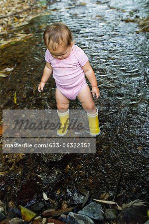 Baby girl wearing rubber boots, wading in stream