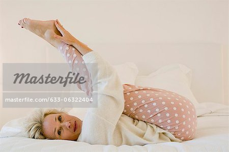 Femme mature sur lit étirement des jambes