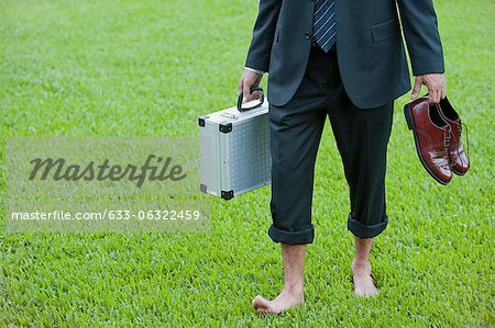 Homme d'affaires de marcher pieds nus sur l'herbe portant des chaussures et des porte-documents