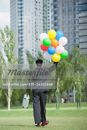 Homme d'affaires marchant avec bouquet de ballons, vue arrière