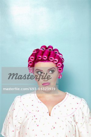 Young woman with curlers on pink hair over colored background