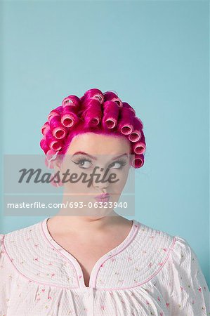 Jeune femme, il le fait avec des cheveux roses et bigoudis sur fond coloré