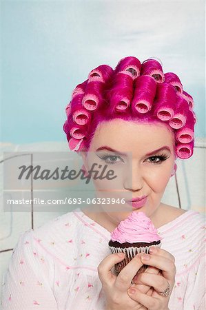 Portrait of a young woman making face while holding cupcake