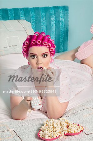 Portrait de femme jeune choquée, regarder la télévision avec pop-corn en position couchée sur le lit