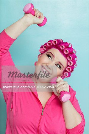 Playful young woman lifting weights over colored background