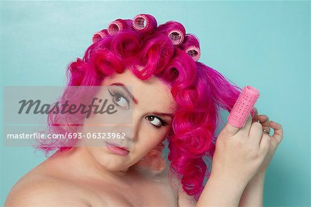 Young woman removing hair curlers over colored background