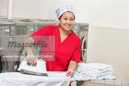 Happy young employee wearing bandana while ironing in Laundromat