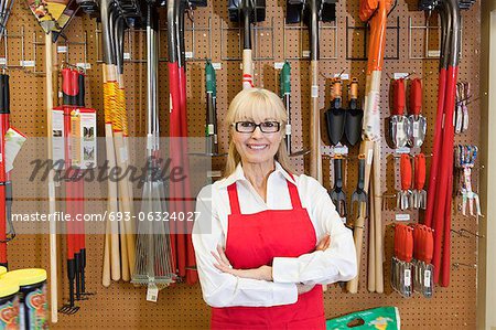 Portrait of a happy senior woman with arms crossed in front of gardening tool