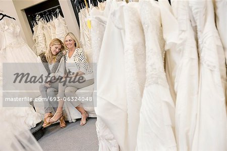 Happy mother and daughter sitting together on sofa in bridal boutique
