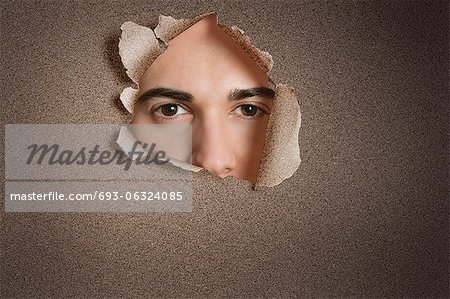 Portrait of a young Caucasian man peeking from ripped paper hole