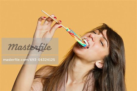 Portrait d'une jeune femme manger sucette sur fond coloré