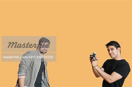 Portrait of young man photographing friend over colored background