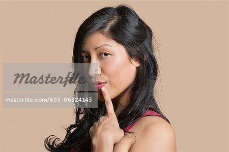 Portrait d'une belle jeune femme posant avec le doigt sur les lèvres sur fond coloré