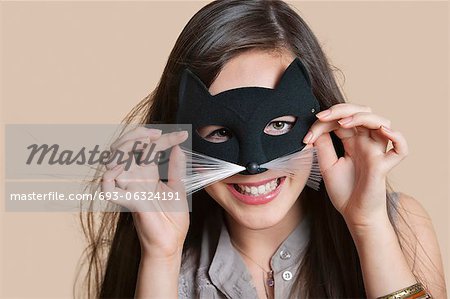 Portrait d'une jeune femme imitant comme chat tout en regardant dans le masque pour les yeux sur fond coloré