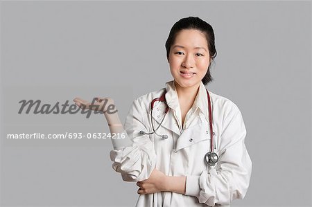 Portrait of an Asian female doctor displaying an invisible product over gray background