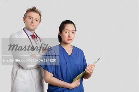 Portrait of a Caucasian doctor standing with an Asian nurse over gray background