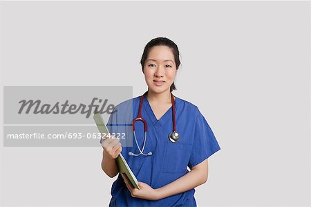 Portrait of an Asian female nurse holding clipboard over gray background