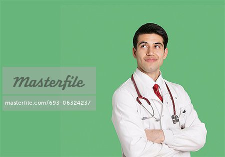 Männlichen Arzt in Laborkittel stehend mit Arme verschränkt, Blick nach oben auf grünem Hintergrund