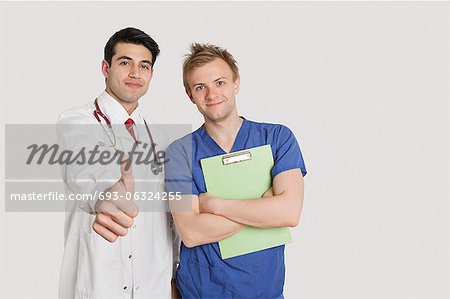 Porträt eines indischen Arztes Gestikulieren Daumen oben stehen mit männliche Krankenschwester über hellgraue Hintergrund
