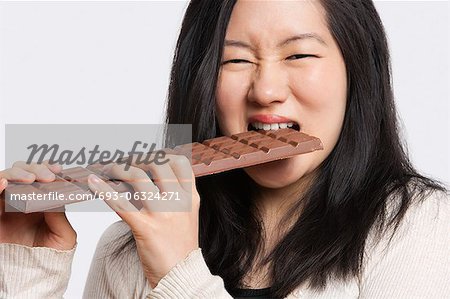 Portrait d'une jeune femme mangeant une grande barre de chocolat sur fond gris clair