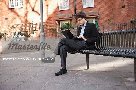 Junger Geschäftsmann mit Laptop beim Sitzen auf Bank